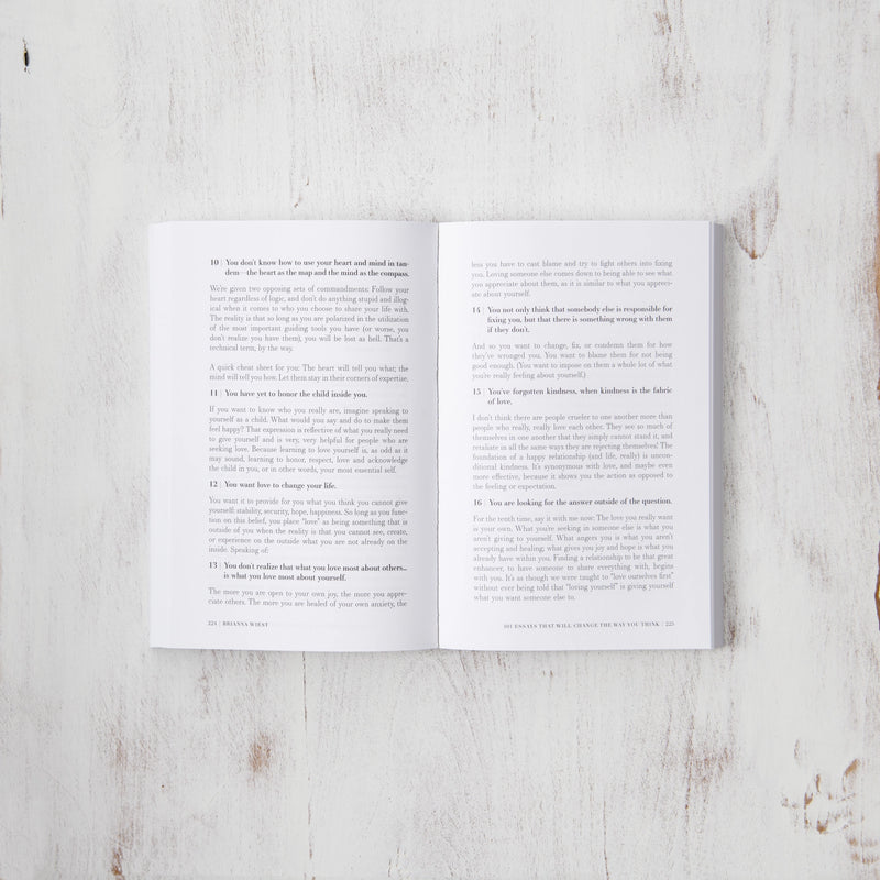 A motivational copy of "101 Essays That Will Change The Way You Think" by Brianna Wiest, published by Thought Catalog, featuring an open page on a wooden surface.