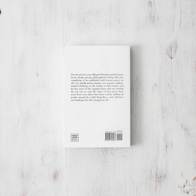 The back of "101 Essays That Will Change The Way You Think | Brianna Wiest" by Thought Catalog, providing inspiration and self-help insights on a wooden surface.