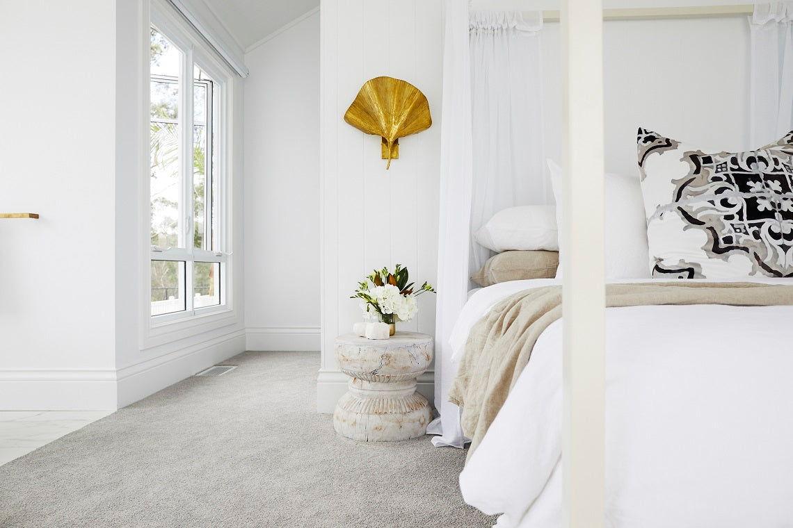 White bedroom corner with a gold wall ornament and a canopy bed