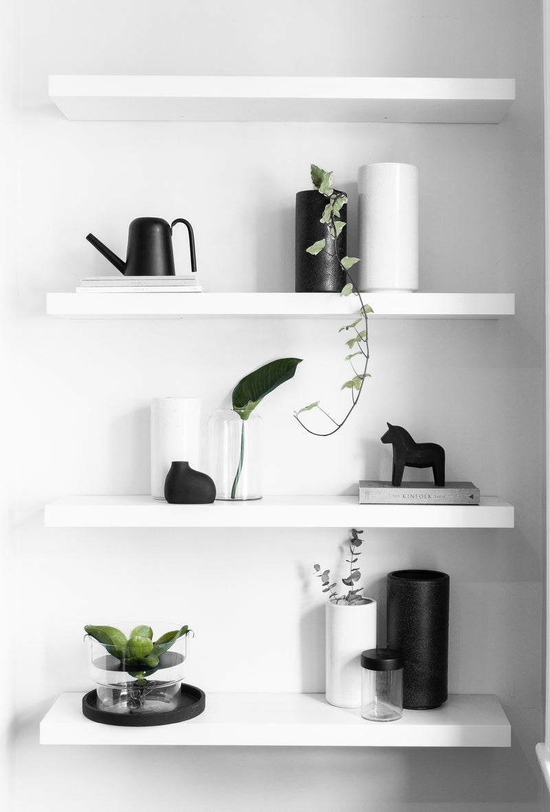 A white shelf adorned with Zakkia handmade blown glass vases, including a Zakkia Deco Vase and a Zakkia Tall Clear vase, alongside vibrant green plants.