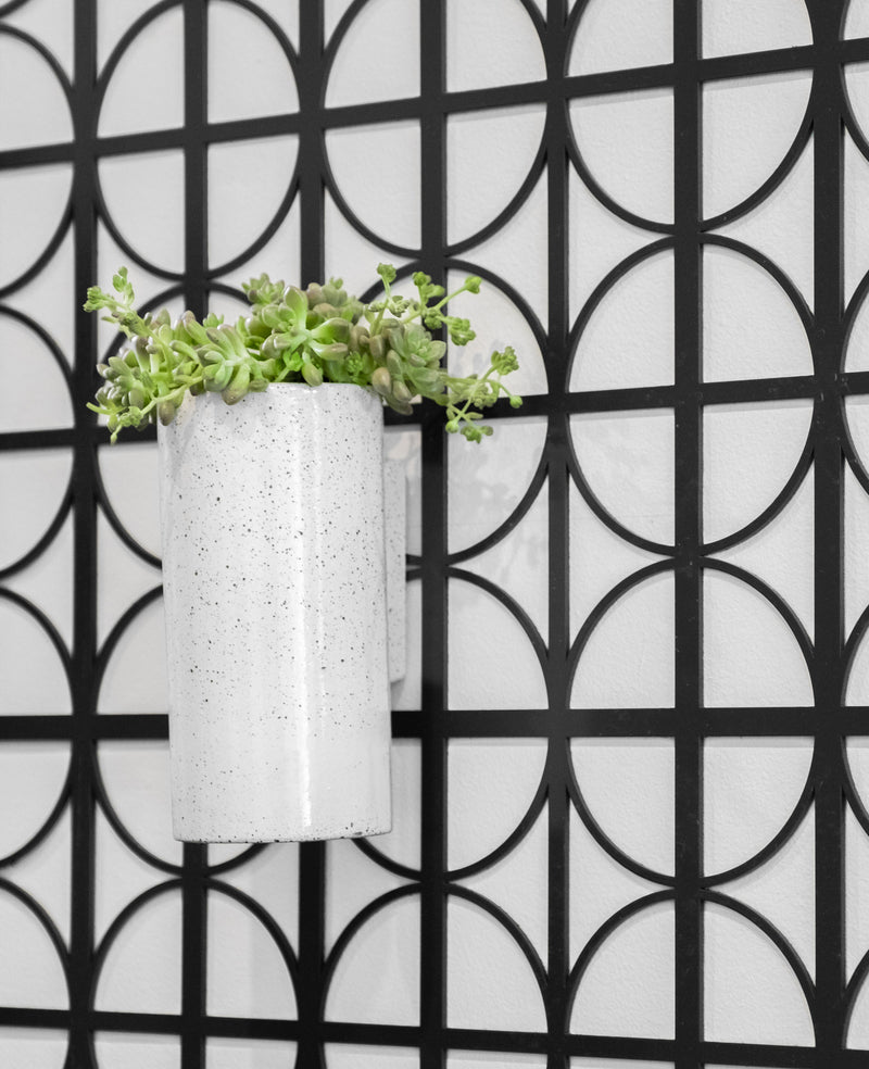 An Embers Wall Planter - Small Ash potted plant, featuring a stunning reactive glaze process, is displayed on a black and white tiled wall. (Brand Name: Zakkia)