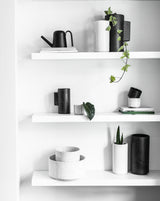 A white shelf with black and white items on it, including Embers Wall Planter - Small Ash outdoor pots with a reactive glaze process from Zakkia.