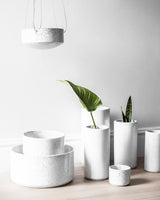 Zakkia's Embers Wall Planter - Small Ash featuring a group of white vases and a plant on a wooden table, showcasing the exquisite reactive glaze process.