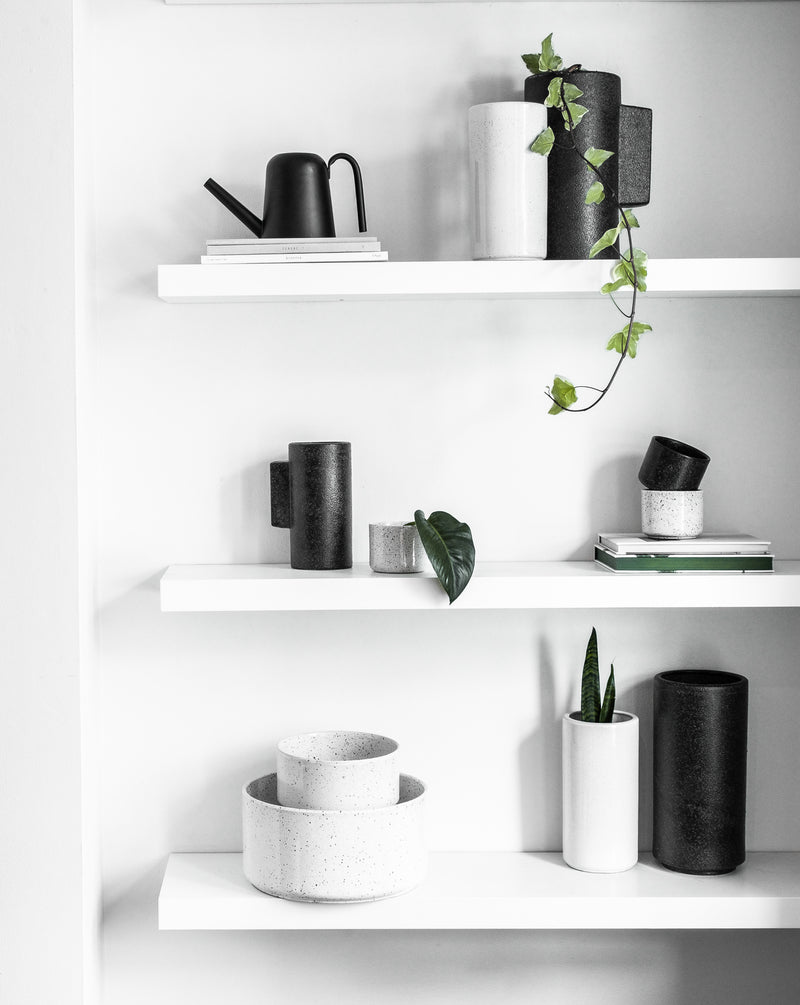 A Zakkia shelf with black and white items, including Embers Bowl Planter - Medium Charred pots and plants, featuring an organic finish.