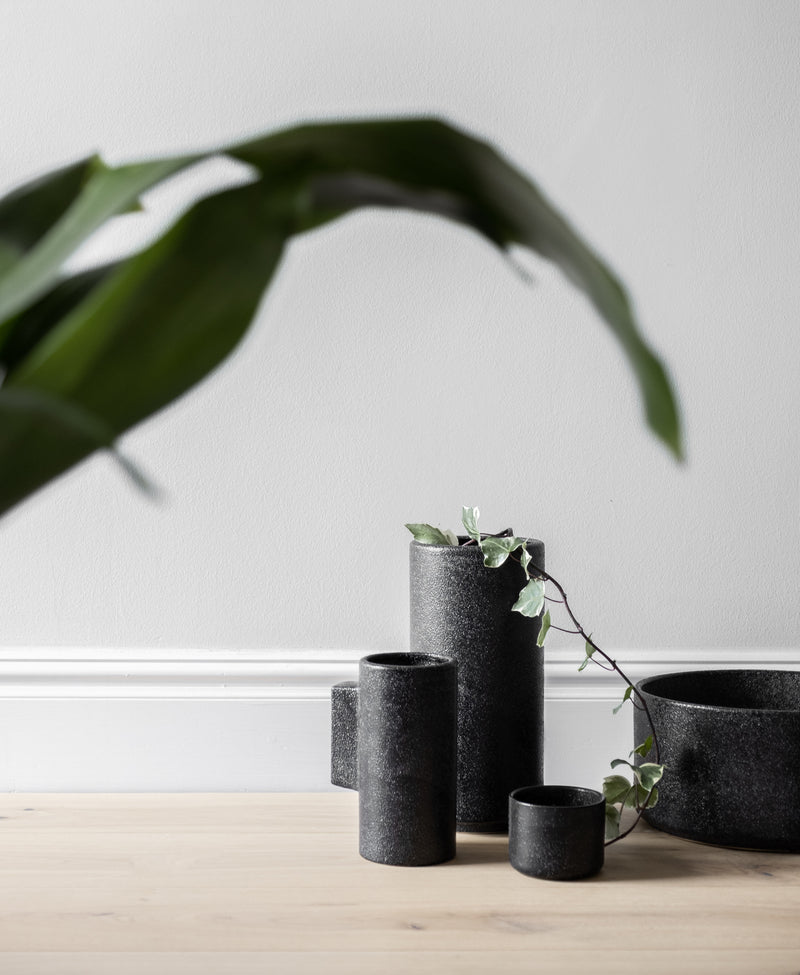 An Embers Hanging Planter - Small Charred by Zakkia sits on a wooden table next to a plant.