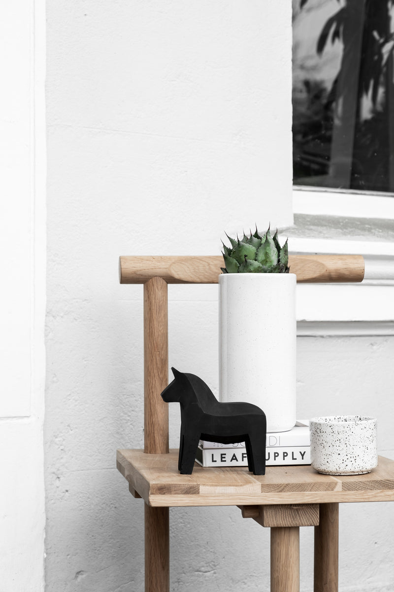 A black and white photo of a wooden chair with a plant on it, featuring the Zakkia Embers Hanging Planter - Small Charred.