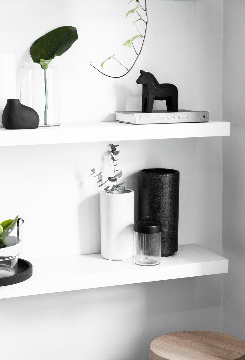 An Embers Wall Planter - Large Charred adorned with black and white vases featuring a reactive glaze finish, accompanied by a stool. (Brand Name: Zakkia)