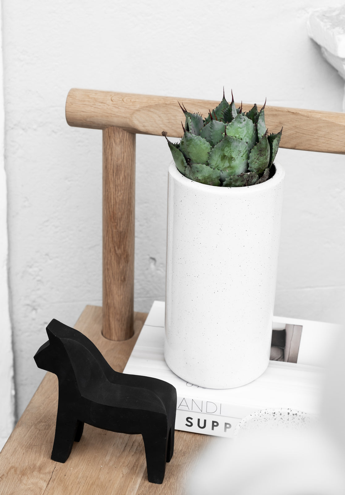 A black Zakkia horse standing on a Embers Table Planter - Small Charred next to a potted plant with an organic finish.