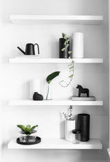 A white shelf adorned with black and white vases and plants, including Embers Wall Planter - Small Ash from Zakkia that showcase a stunning reactive glaze process.