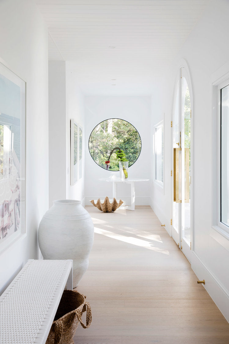 Long white hallway with a round window, urn and bench