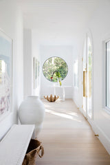 A white hallway with a large round window, showcasing Three Birds Renovations: Dream Home How-To goodness in home transformations.