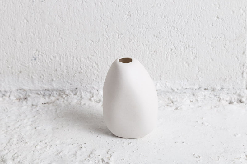 A Harmie Vase - Seed Grey, handmade by talented Vietnamese artisans, adorns a concrete wall with its elegant presence. The vase's white surface beautifully contrasts with the raw texture of the wall, while Ned Collections