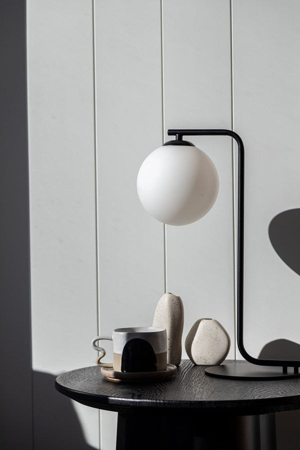 A Bella May table lamp by Ned Collections on a table next to a cup of coffee.