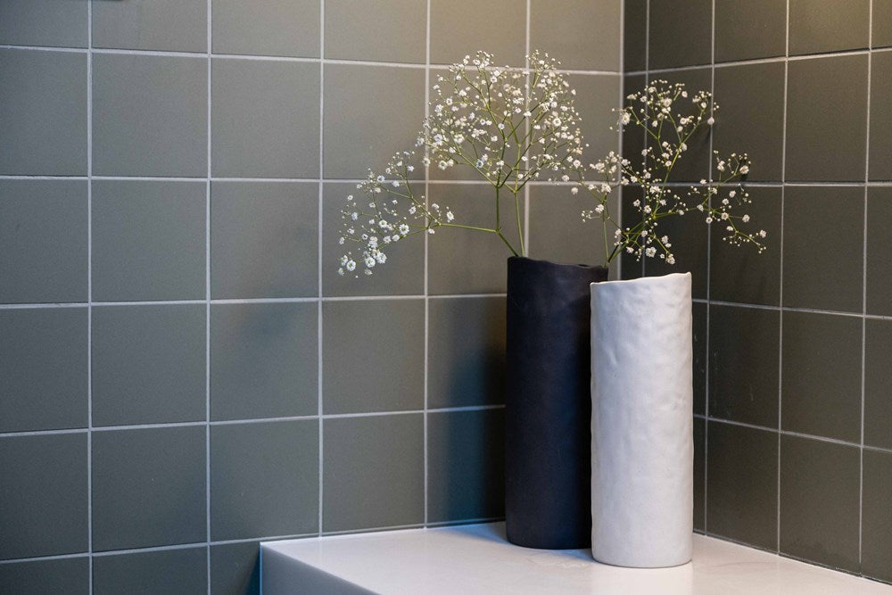 Two Bernie Vases from Ned Collections, with flowers in them, sit on a gray tiled wall.