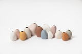 A group of different colored Harmie vases, crafted by Vietnamese artisans, arranged on a white surface.