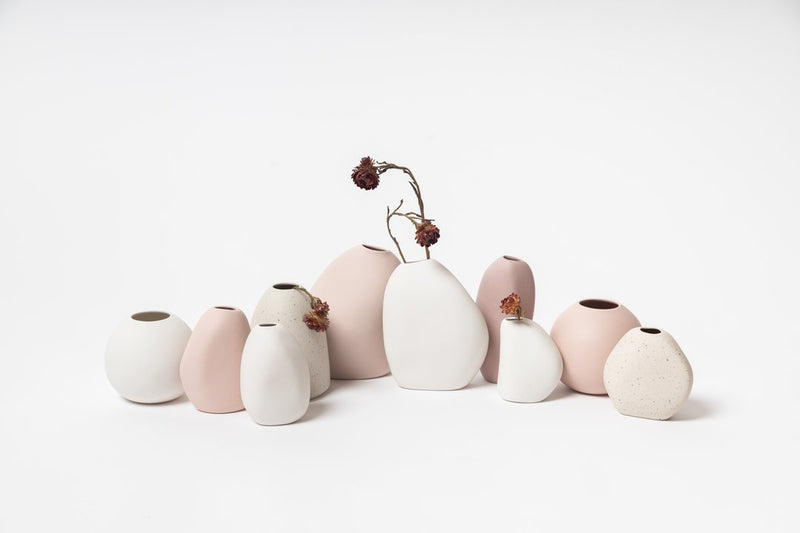 A collection of Ned Collections Harmie vases, handmade by Vietnamese artisans, featuring organic seed-like shapes on a white surface.