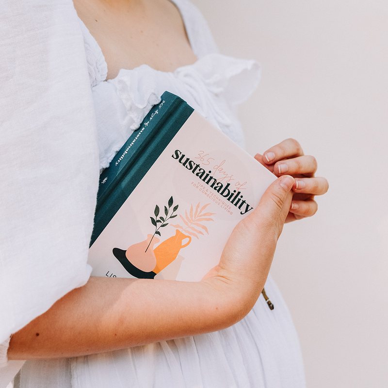 A Scandinavian-inspired woman showcases her book on sustainable decorating and styling called "365 Days of Sustainability" by Collective Hub.