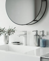 A bathroom in the Junip collection with a white sink and a mirror above it would include the Junip Soap Pump - Stainless Steel from Umbra.