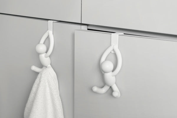 Two white Umbra Buddy Over the Door Hook Sets of 2 hanging on a cabinet door.