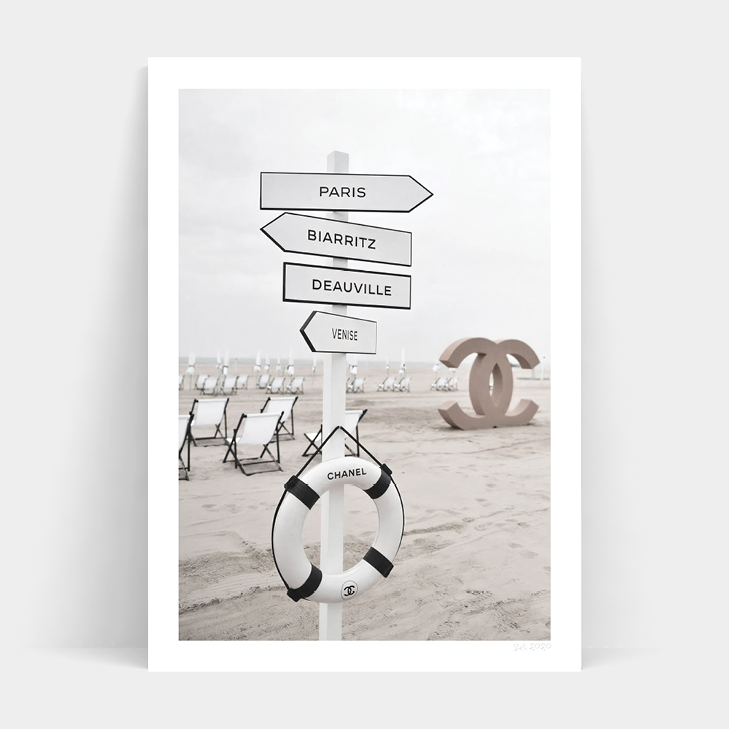 A black and white photo of a beach sign with a life preserver on it, featuring the CHANEL BEACH CLUB by Art Prints.