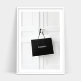 Black Chanel Addict shopping bag hanging on a white door.