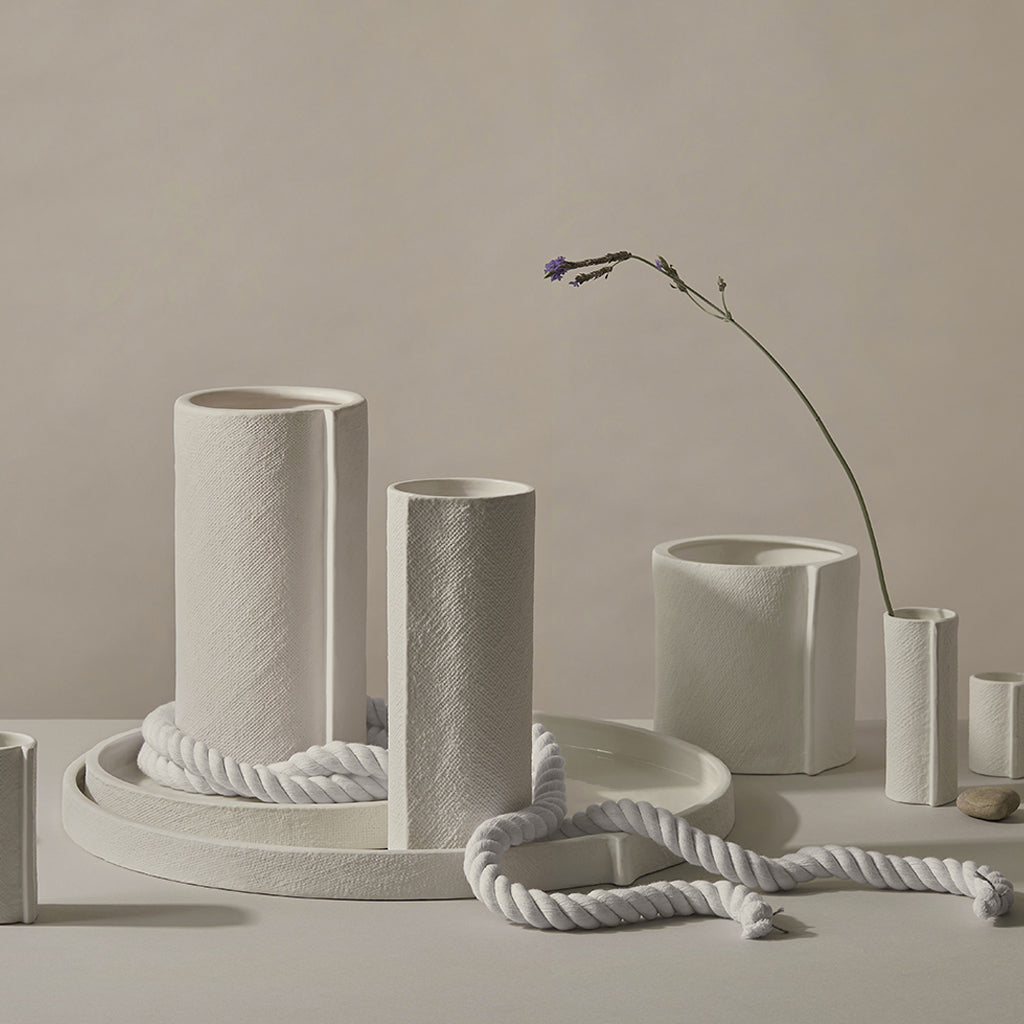 Off white ceramic vases, pots and trays grouped on a table against a taupe wall
