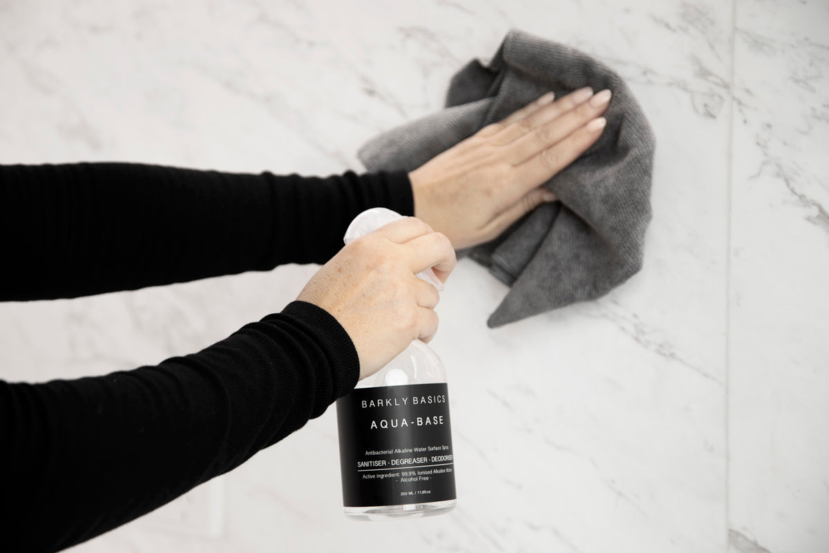A woman using Barkly Basics grey microfibre cloths to chemical free clean a marble wall.