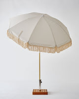 A lightweight Brel Club Fringe Umbrella - Palm Tree with tassels on a wooden stand, combining durability and style.
