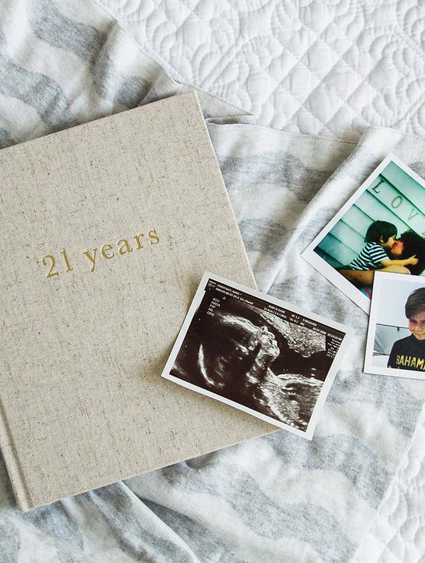 A 21 Years - 21 Years Of You journal filled with memories captured through photos, including a heartwarming image of a baby lying on a bed by Write To Me.