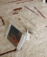 A Magino Stool With Magazine Rack - Clear Acrylic by Umbra is sitting on top of a coffee table.