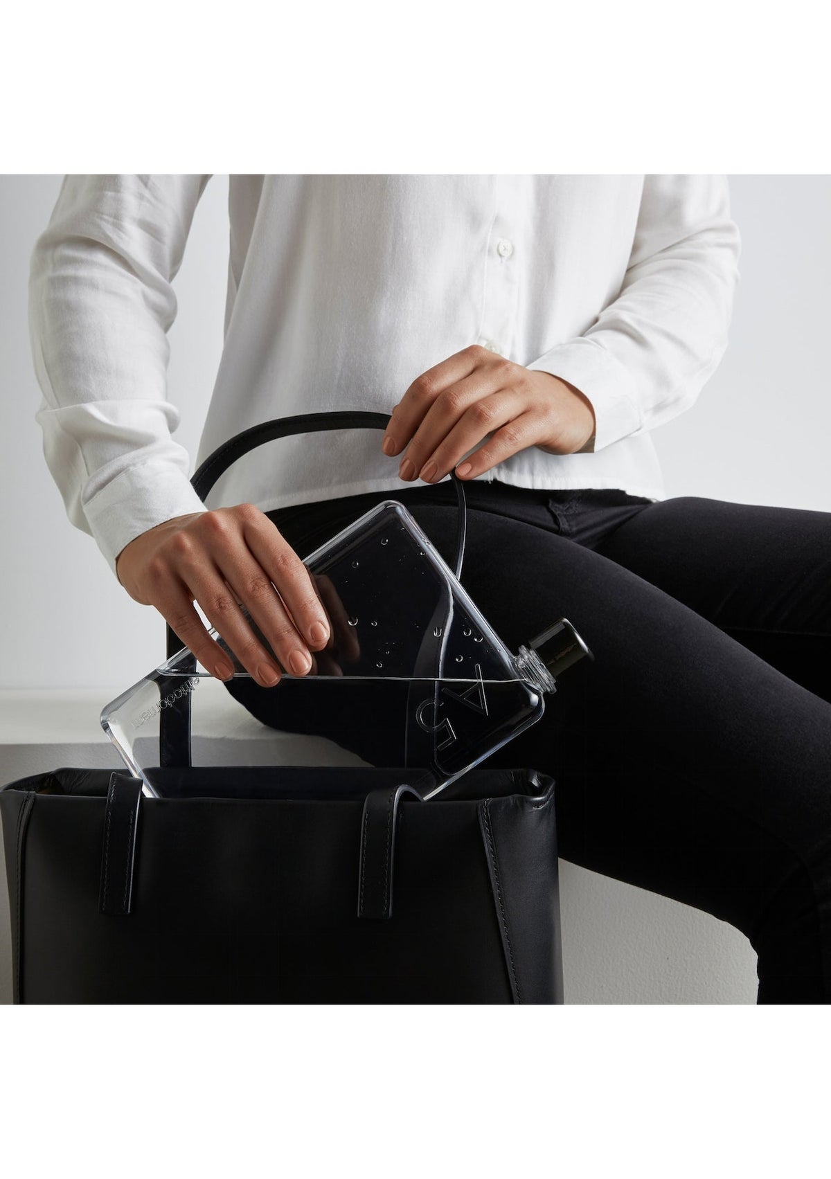 Memobottle slim flat bottle held by a seated woman in black beside a leather tote