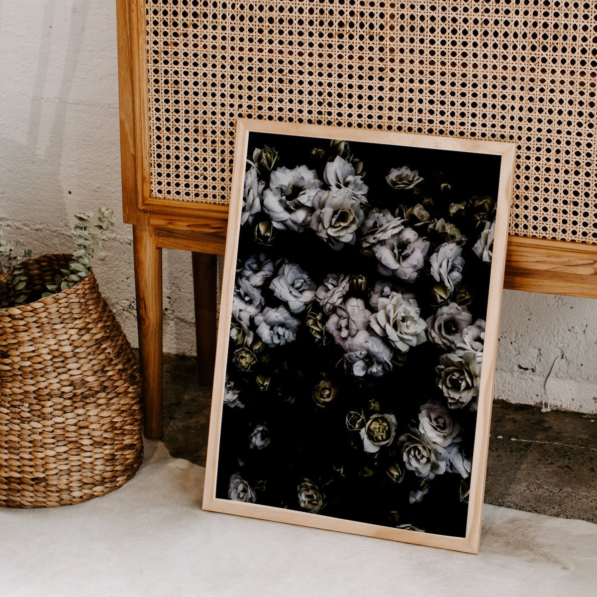White Flowers print in a timber frame leaning by a cane headboard and a basket