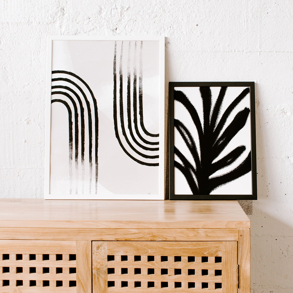 Abstract Leaf print in a black frame leaning beside an arch print on a rattan cabinet