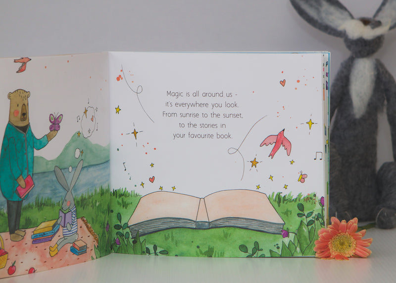 In a World Full of Magic open to a watercolour spread of an open book and flowers, beside a plush bunny