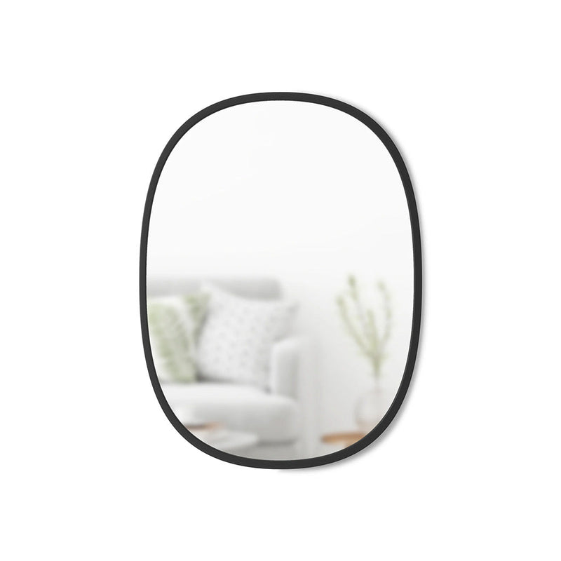 The Hub Mirror Oval - Black, part of the Umbra range, features a sleek black design with a rubber rim. This stylish mirror is the perfect addition to any living room.