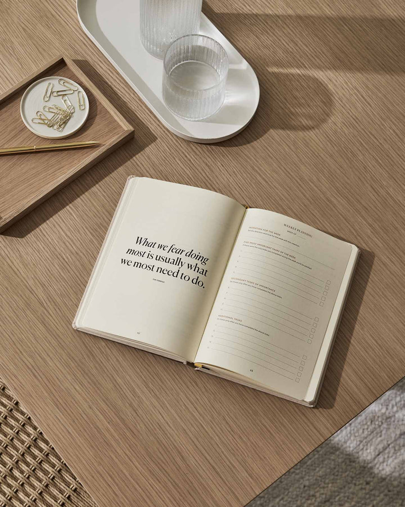 An Intelligent Change Productivity Planner open on a wooden table with a glass on it.