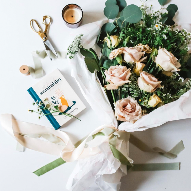 A Scandinavian-inspired homeware decor featuring a bouquet of 365 Days of Sustainability by Collective Hub complemented with scissors and a book.