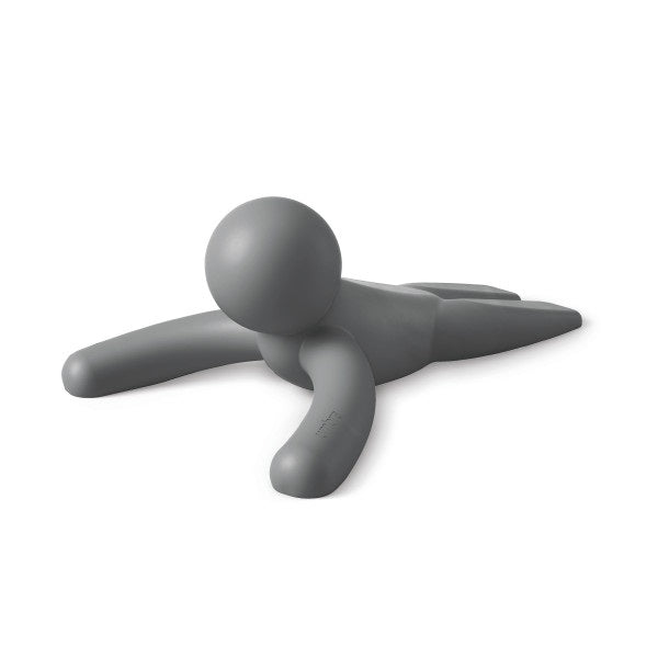 An Umbra Buddy Doorstop Charcoal figure laying down on a white surface.