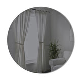 A Hub Mirror - Bevy 36" - Smoke from the Umbra range, placed in a room adorned with white curtains and a plant.