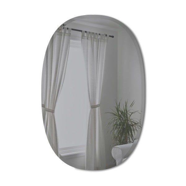 A Hub Mirror - Bevy Oval 24X36 - Smoke by Umbra hangs on a wall in a room adorned with elegant curtains and complemented by a lush plant.