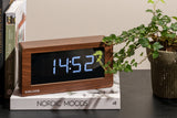 A Karlsson Boxed LED - Various Options alarm clock sits on a table next to a plant.