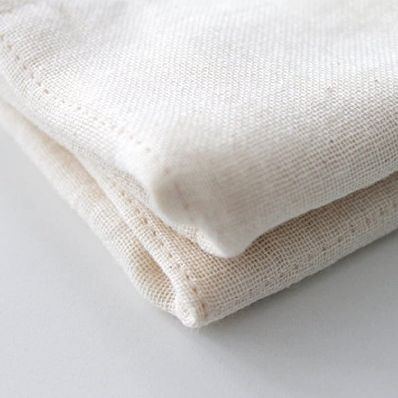 A NAWRAP ORGANIC MINI TOWEL - IVORY, made by Flux Home, folded on top of a sensitive skin-friendly white surface.