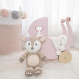 A Whimsical Knitted Toy (Ava the Fawn) from Living Textiles is sitting next to a pink stroller.