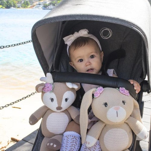 A baby in a stroller with two Living Textiles Whimsical Knitted Toy (Ava the Fawn) stuffed animals.