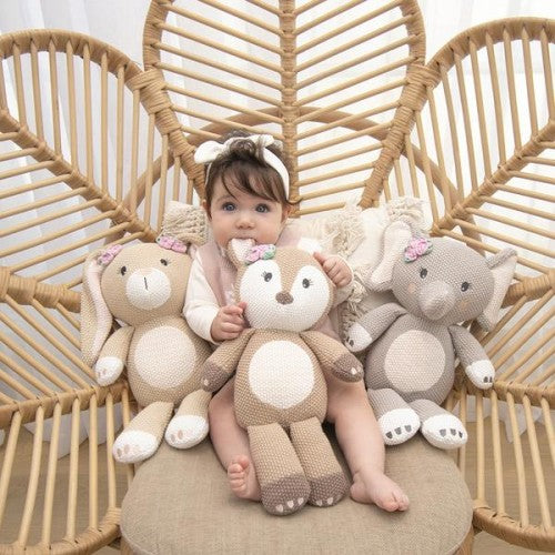 A baby is sitting in a wicker chair with three Living Textiles Whimsical Knitted Toy (Ava the Fawn).