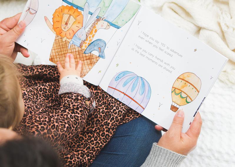 A child is reading the book MY WISHES FOR YOU by Olive + Page about hot air balloons.