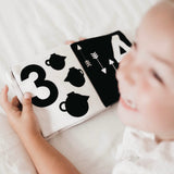 A little girl holding a My Numbers | Luxe Soft Cover Book by My Family Book with high contrast images of numbers.