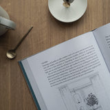 A successful book, "The Interior Design Handbook" by Frida Ramstedt, is open on a table next to a cup of coffee, adding a professional touch to the interior design.
