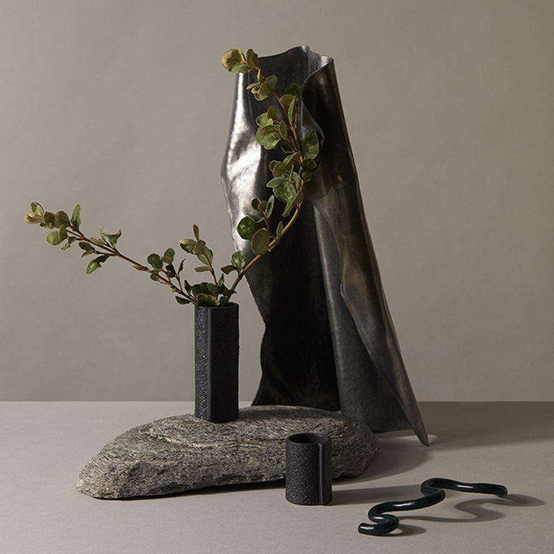 A Zakkia Burlap Vase - Small Black sits on top of a rock.