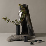 A Zakkia Burlap Vase - Small Black sits on top of a rock.